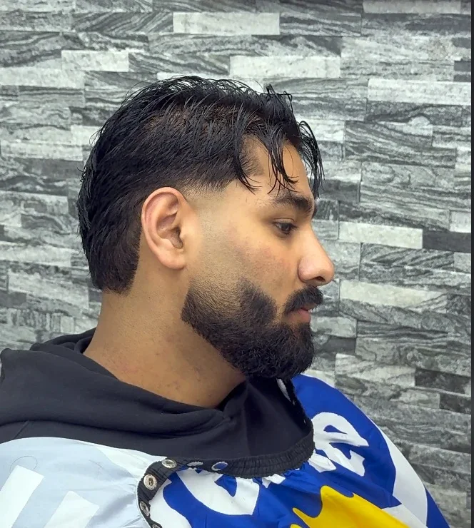 Slicked-back dark hair with a full, shaped beard.